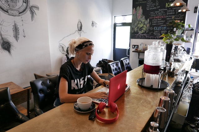 Žena v čiernom tričku KISS sedí v kaviarni a píše na notebooku.jpg