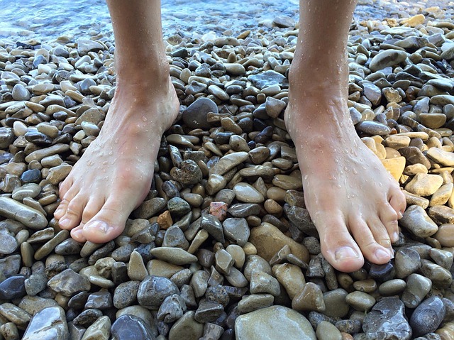Muž s bosými nohami stojí na kamenistej pláži pri vode.jpg